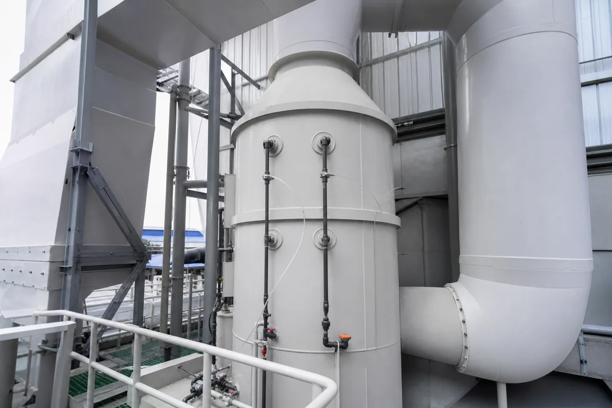 A wet scrubber tower with inlet and outlet ductwork plus pressure sensing lines, photographed from a low three-quarter maintenance-platform angle, no people, no text.