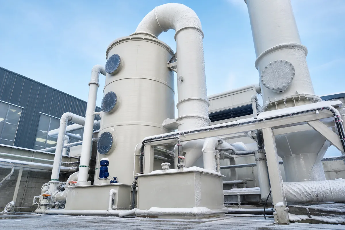 Low-angle winter photograph of an outdoor PP packed-bed scrubber with insulated recirculation piping, heat-trace runs, and frost-covered ductwork against a cold industrial backgrou